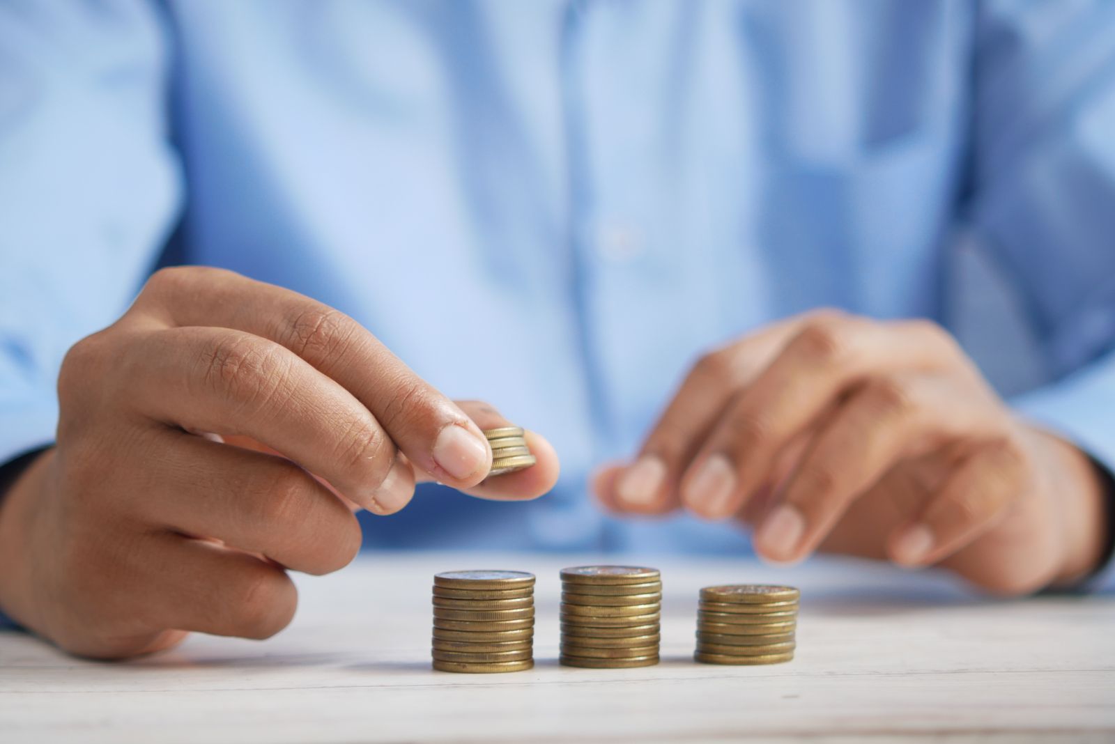 Hands stacking coins in growing columns on a table