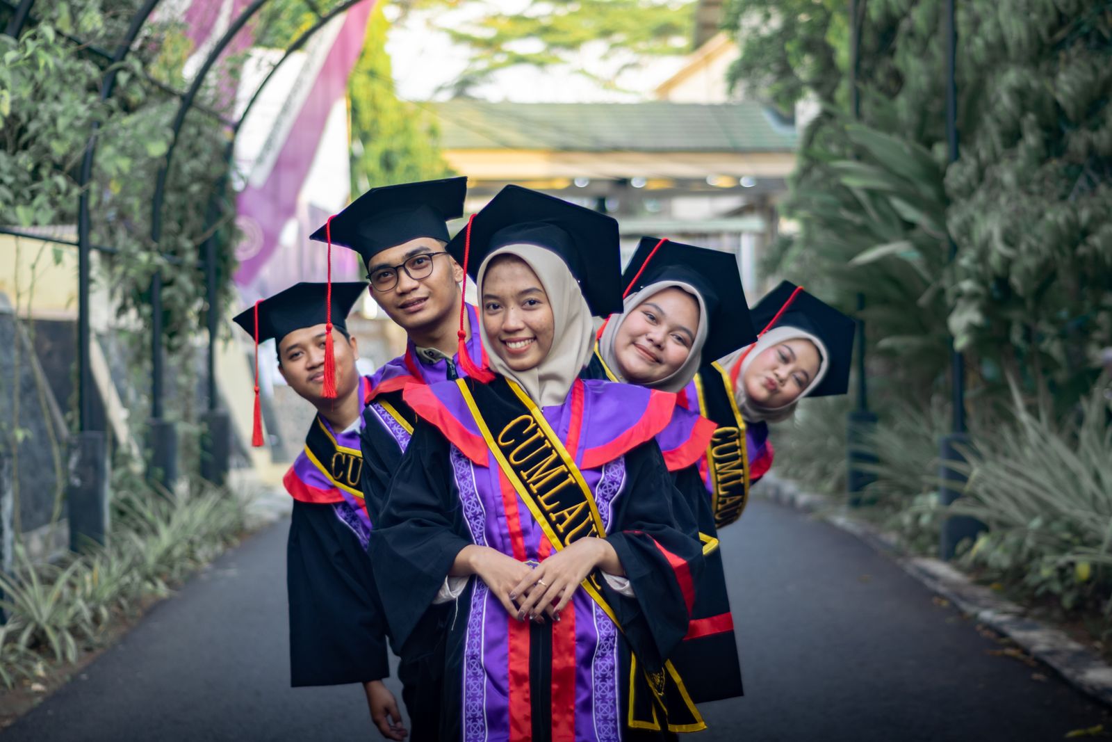 Graduates in caps and gowns smiling on a tree-lined path