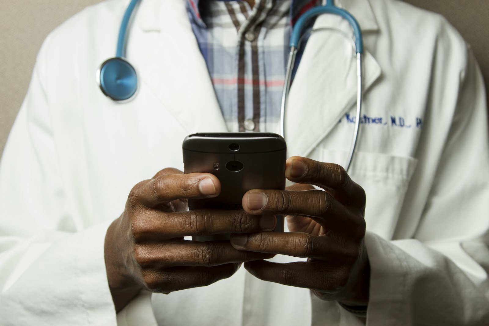 A doctor in a white coat holding a phone, stethoscope around the neck