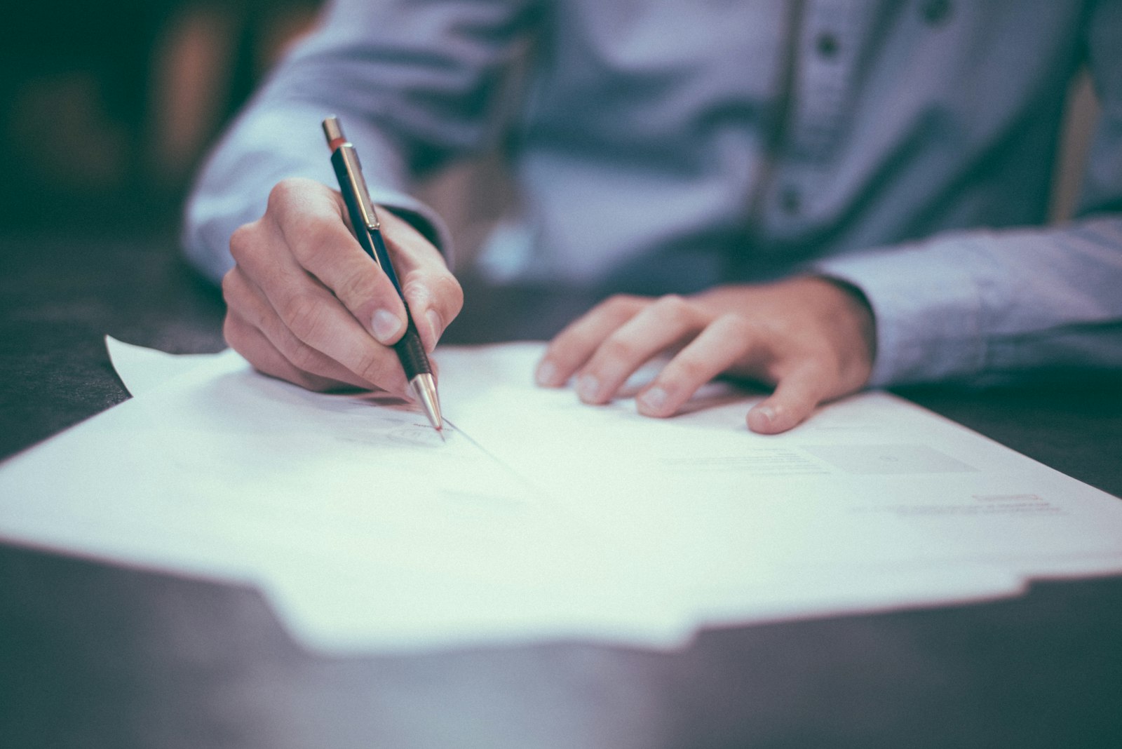 A person signing documents at a desk with a pen